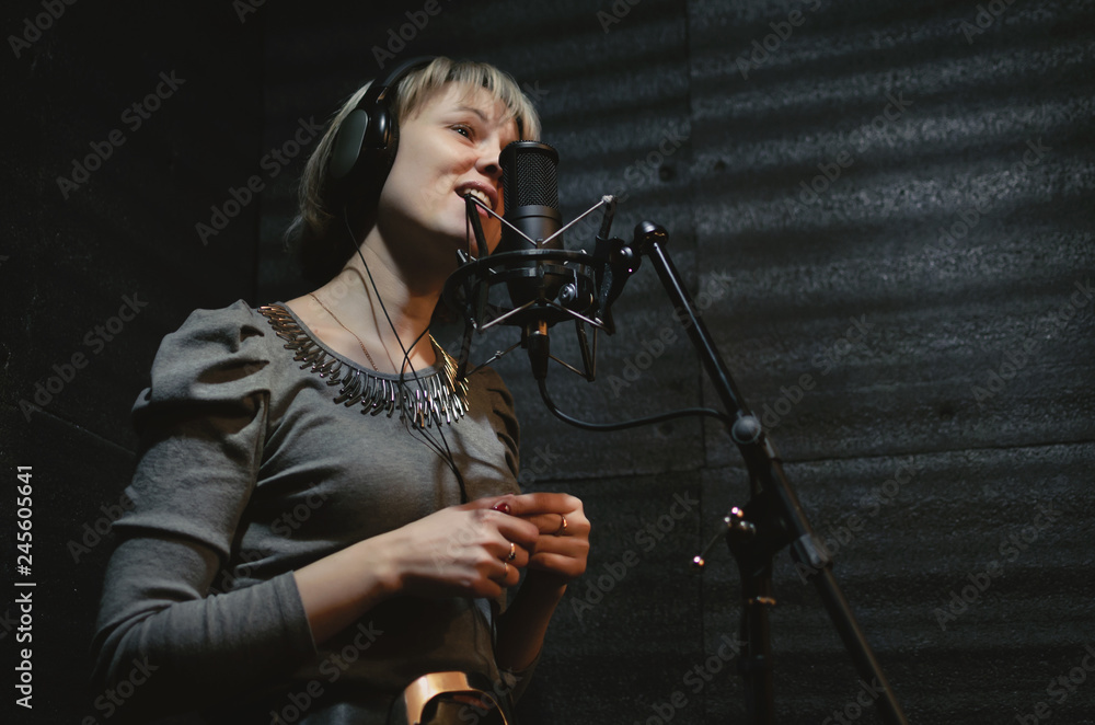 Naklejka premium Woman a singer in a headphones is performing a song in a sound recording studio and is standing in front of the microphone.