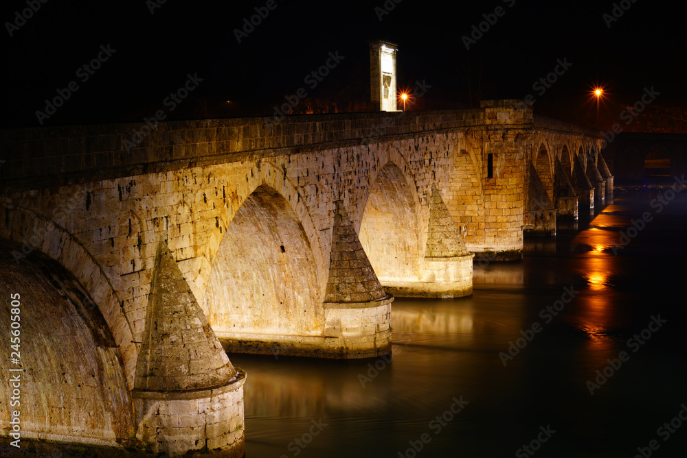 View of the famous landmark Visegrad (Bosnia and Herzegovina) - an ancient arched bridge at night with illumination.
