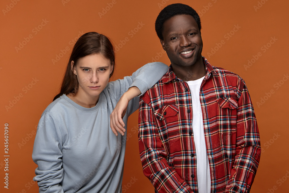 Picture of happy best friends European woman and dark skinned man in stylish clothes enjoying leisure time together indoors, posing against blank orange copyspace wall background, guy laughing Picture of happy best friends European woman and dark skinned man in stylish clothes enjoying leisure time together indoors, posing against blank orange copyspace wall background, guy laughing