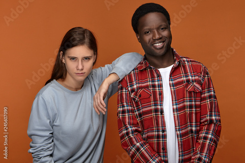 Picture of happy best friends European woman and dark skinned man in stylish clothes enjoying leisure time together indoors  posing against blank orange copyspace wall background  guy laughing