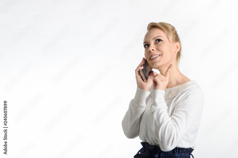 20-years blond girl in white blouse and blue skirt on white background talking on the cell phone 20-years blond girl in white blouse and blue skirt on white background talking on the cell phone