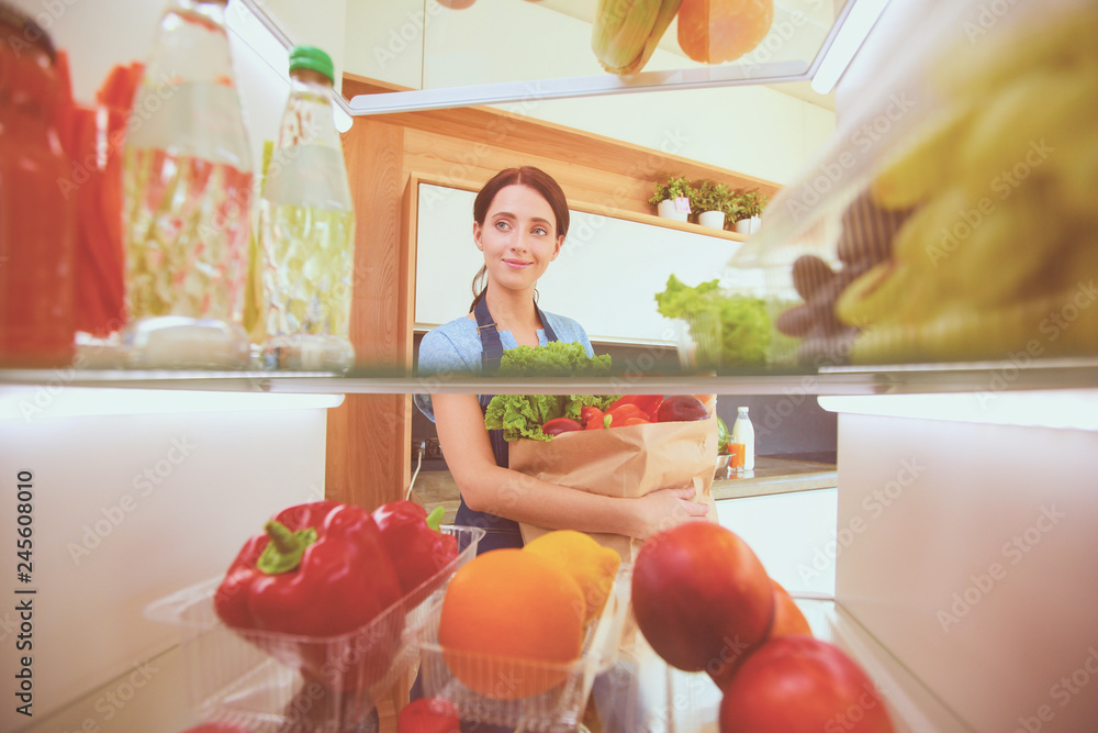Portrait of female standing near open fridge full of healthy food, vegetables and fruits. Portrait of female Portrait of female standing near open fridge full of healthy food, vegetables and fruits. Portrait of female
