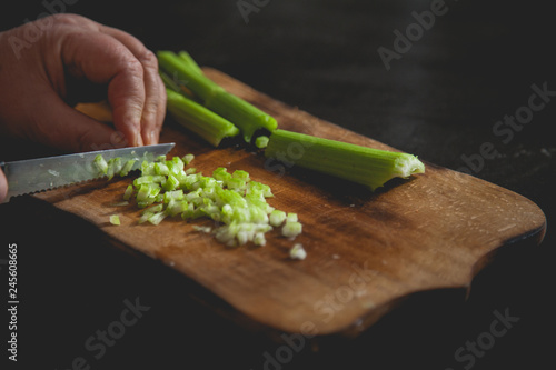 Woman preparing food in her kitchen, she is chopping fresh celery on a cutting board with a knife on the tray