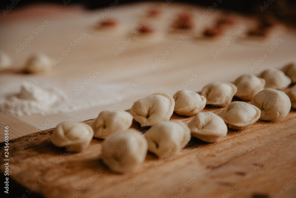 Uncooked russian pelmeni on cutting board and ingredients for homemade pelmeni on white table. Process of making pelmeni, ravioli or dumplings with meat