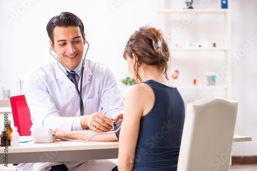 Young doctor checking woman's blood pressure