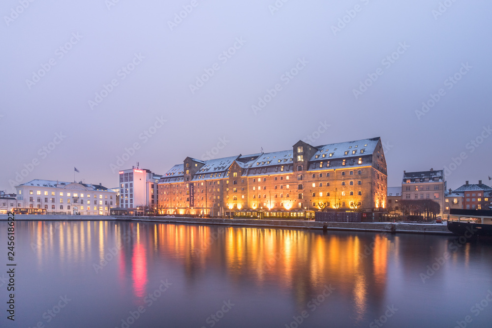 View of Admiral Hotel in Copenhagen during sunset with reflection in the water, seen from the shore.