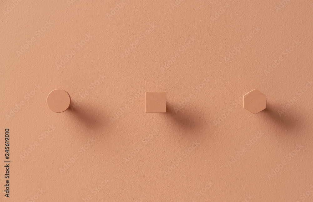 Metal orange hangers in forms of circle and square and hexagon on colorful wall in studio Metal orange hangers in forms of circle and square and hexagon on colorful wall in studio