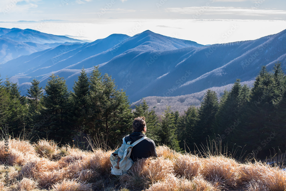 One man hiker wearing vintage rucksack sitting alone admiring the mountain landscape in winter.