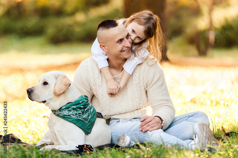 Happy father and daughter with dog labrador is having fun are sitting on green grass in park. Happy father and daughter with dog labrador is having fun are sitting on green grass in park.
