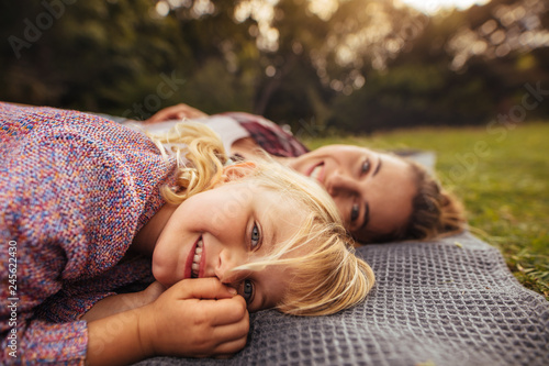 Little girl lying on picnic plaid with mother at back photo