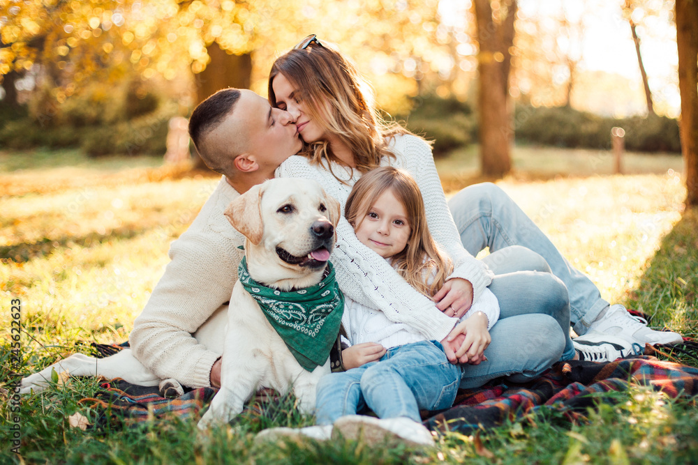 Fototapeta premium Happy beautiful family with dog labrador is having fun are sitting on green grass in park.
