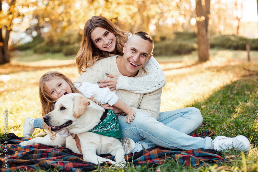 Fototapeta premium Happy beautiful family with dog labrador is having fun are sitting on green grass in park.