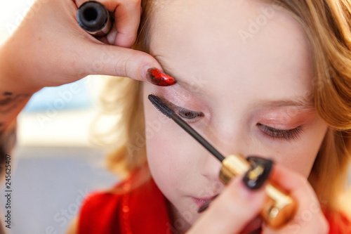 Hand of makeup master applying mascara for little pretty girl model