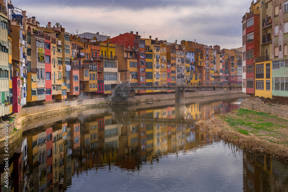 Colorful yellow, red, green houses alongside the Onyar river with reflection on the water in Girona Catalonia region Spain