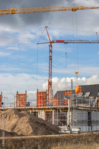 Baustelle mit Bauarbeitern und Kran an dem ein Betonkübel hängt.