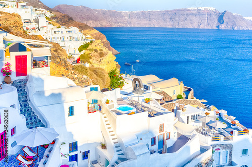 Famous European Destinations. Breathtaking View of Classic White Roofed Houses and Pastel-Blue Colors of Oia Village on Santorini Island in Greece With Boats in Background.