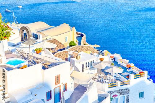 Famous European Destinations. Breathtaking View of Classic White Roofed Houses and Pastel-Blue Colors of Oia Village on Santorini Island in Greece With Boats in Background.