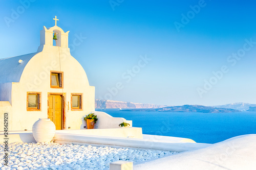 Beautiful Classic White Roofed Church With Flat Pediment and Bell Against Volcanic Caldera on Oia Island in Santorini in Greece.