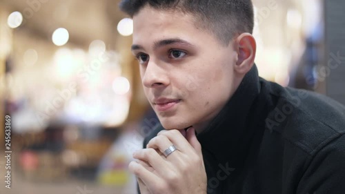 Young man sitting in a modern mall with raised collar feeling cold in slo-mo 