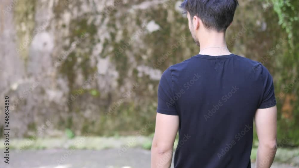 Handsome young man walking down narrow town street or alley, looking away to a side Handsome young man walking down narrow town street or alley, looking away to a side