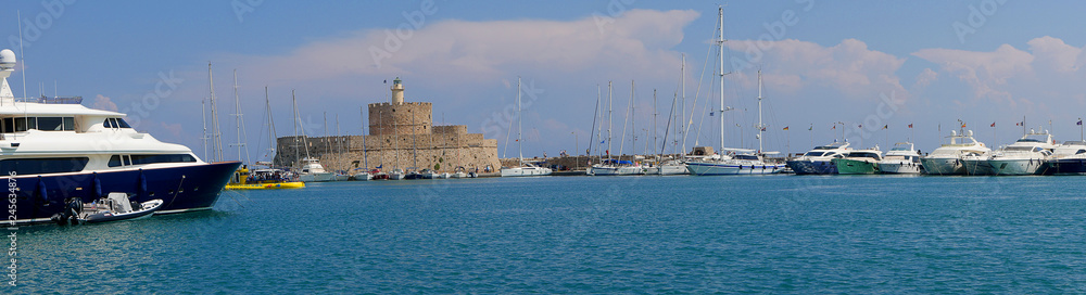 These 3 windmills stand on the Mandraki harbor wall with the fort of St Nikolas on the Greek island Of Rhodes