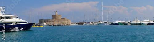 These 3 windmills stand on the Mandraki harbor wall with the fort of St Nikolas on the Greek island Of Rhodes