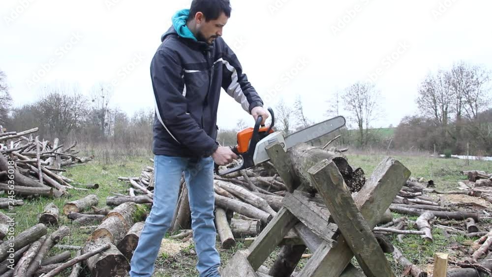 young man cutting wood for fire with a professional chainsaw young man cutting wood for fire with a professional chainsaw