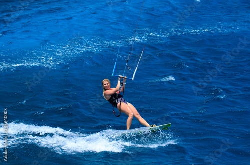 Kite surfing girl in sexy swimsuit with kite in sky on board in blue sea riding waves with water splash. Recreational activity, water sports, action, hobby and fun in summer time. Kiteboarding sport