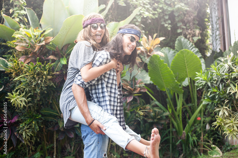 Obraz premium handsome man carrying beautiful girl on back , woman hugging guy. Hippie and gypsy style. they are wearing sunglasses and bandanas