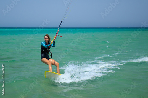 Kite surfing girl in sexy swimsuit with kite in sky on board in blue sea riding waves with water splash. Recreational activity, water sports, action, hobby and fun in summer time. Kiteboarding sport © yanamavlyutova