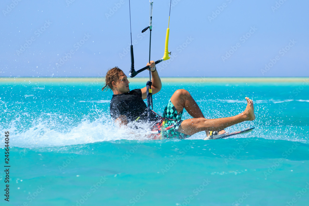 Kite surfing man surf sportsman with kite in sky on board in blue sea riding waves with water splash. Recreational activity, water sports, action, hobby and fun in summer time. Kiteboarding sport