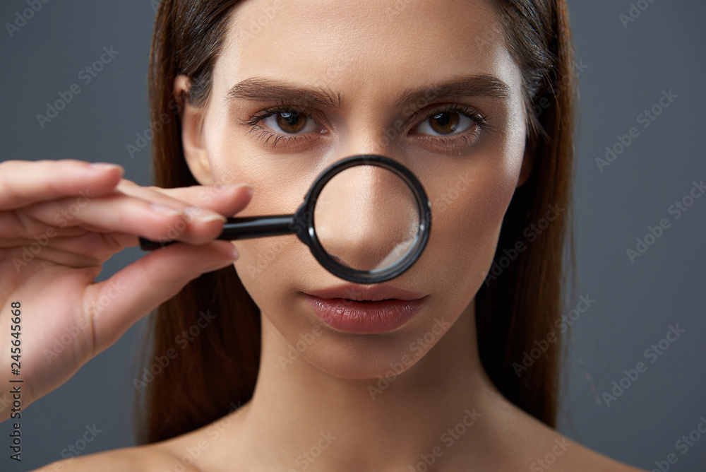 Beautiful young lady examining skin with magnifying glass Beautiful young lady examining skin with magnifying glass