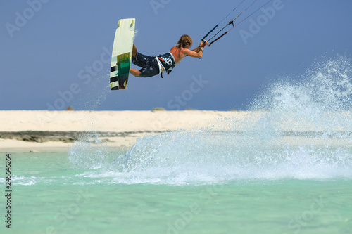 Professional kite boarding rider sportsman with kite in sky jumps high acrobatics kiteboarding trick with grab of kiteboard and huge water splash. Recreational activity, extreme active air sports