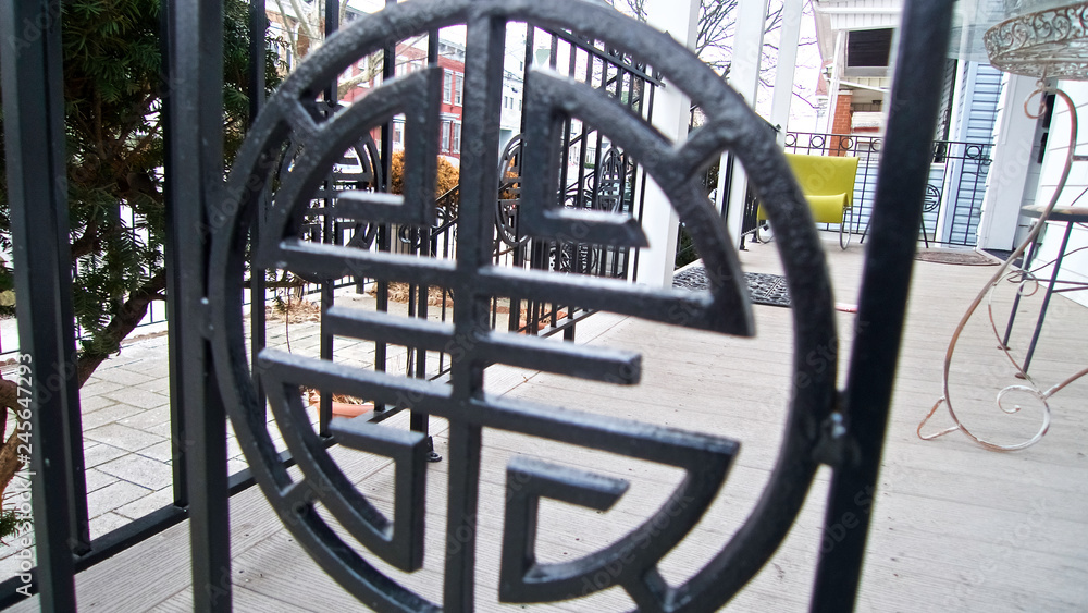 A close-up of the docorative portion of the metal rail of a balcony of a suburban house looking out into the neighborhood street.