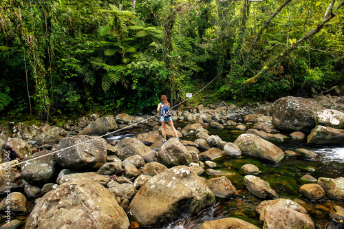 Young woman crossing stream on a trail to Middle Tavoro Waterfalls in Bouma National Heritage Park, Taveuni Island, Fiji