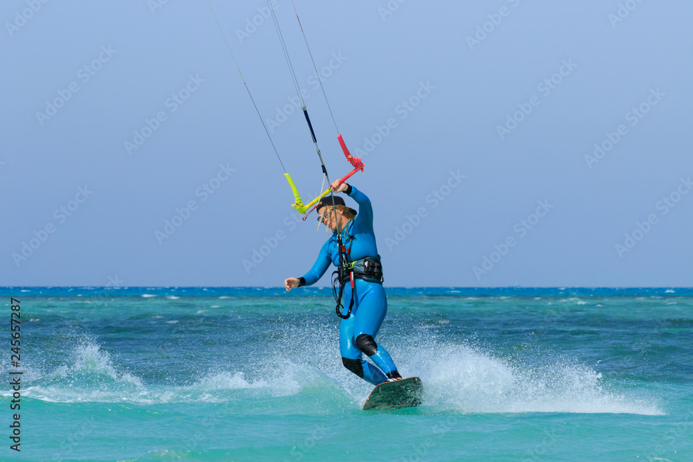 Kite surfing girl in sexy swimsuit with kite in sky on board in blue sea riding waves with water splash. Recreational activity, water sports, action, hobby and fun in summer time. Kiteboarding sport