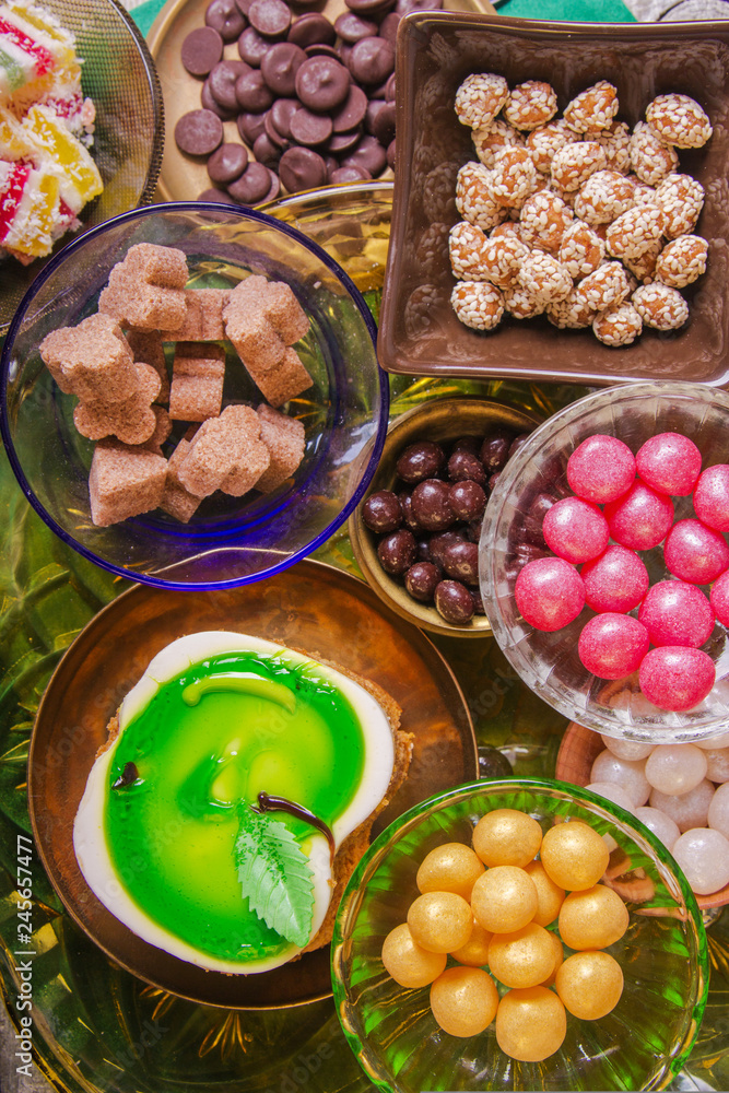 Tea break with a delicious honey cake decorated in the form of a green apple and a variety of multi-colored small candies. Copper and clay plates in a composition with jugs. Arab concept