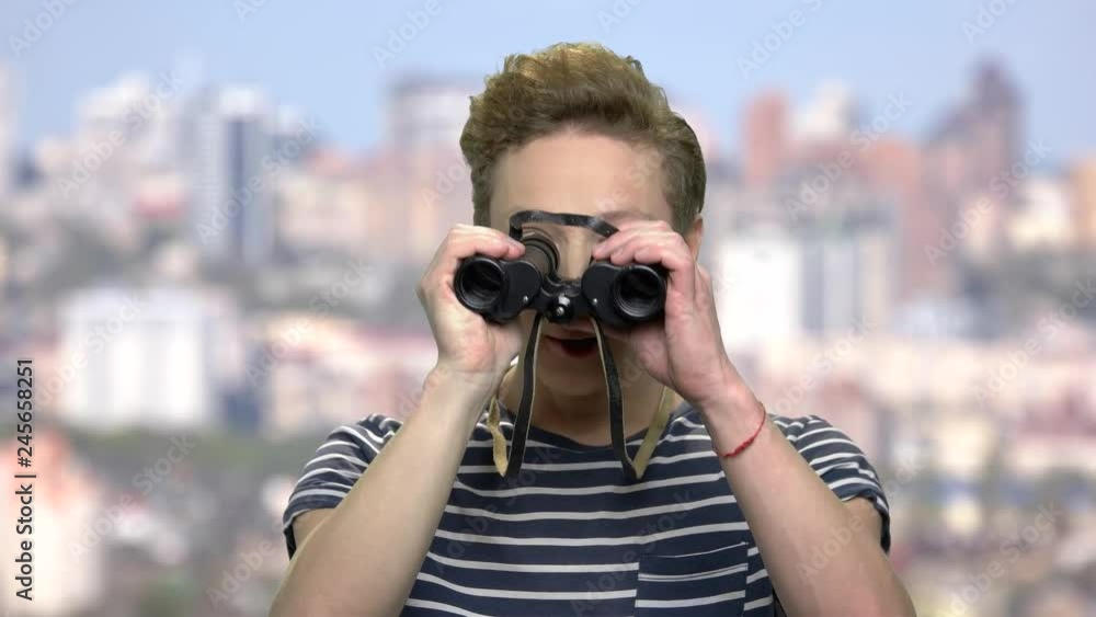 Curious teen boy using binoculars. Excited teen guy watching something with binoculars. Blurred city background. Curious teen boy using binoculars. Excited teen guy watching something with binoculars. Blurred city background.