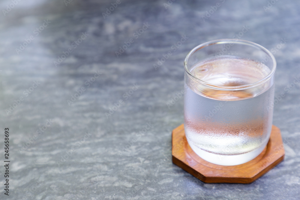 Glass of cool water with wood coaster on gray stone table in coffee shop. Glass of cool water with wood coaster on gray stone table in coffee shop.