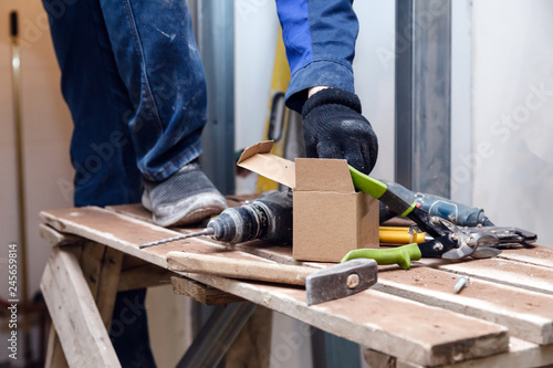 Worker in blue dirty uniform, scaffolding, construction tools, puncher, level, against background of construction site and renovation in kitchen of restaurant