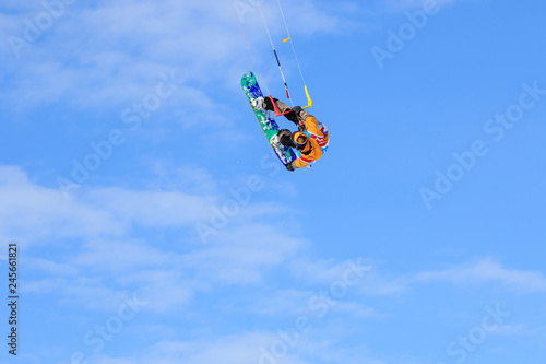 Professional kite boarding rider sportsman with kite in sky jumps high acrobatics kite boarding trick with grab of kite board. Recreational activity, extreme active sports, snow kiting ski snowboard