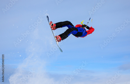 Professional kite boarding rider sportsman with kite in sky jumps high acrobatics kite boarding trick with grab of kite board. Recreational activity, extreme active sports, snow kiting ski snowboard
