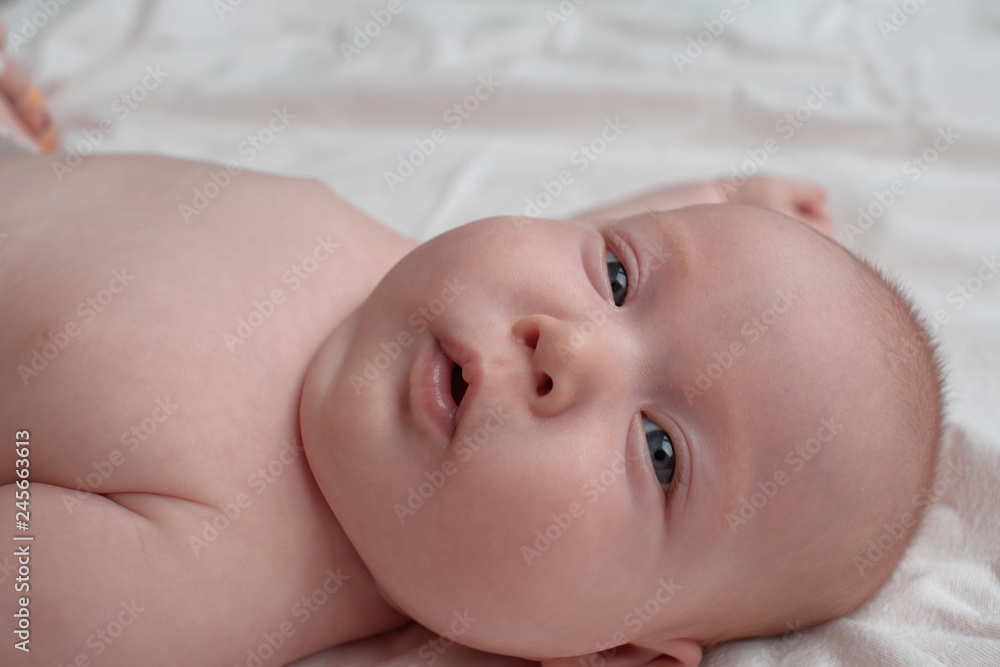 Baby with a surprised face with open mouth. The baby lies on a white linen cloth. Baby with a surprised face with open mouth. The baby lies on a white linen cloth.
