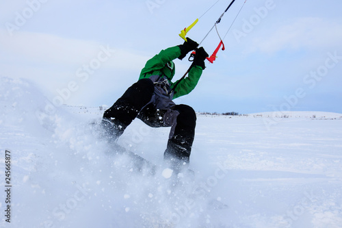 Professional kite boarding rider sportsman with kite in sky jumps high acrobatics kiteboarding trick with grab of kiteboard. Recreational activity, extreme active sports, snow kiting ski snowboard