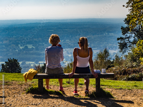 LEITH HILL, DORKING, SURREY, ENGLAND - OCTOBER 10, 2018: Two women on a bench drinking and looking at the view across the Surrey Countryside on a sunny autumn day