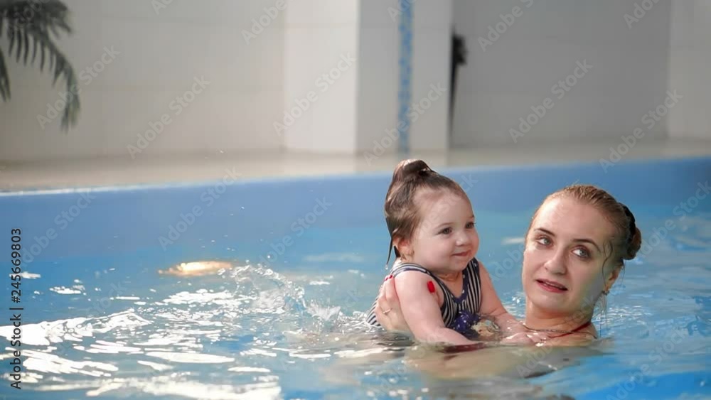 Young mom in the pool playing with her baby daughter in slow motion. Sports family engaged in an active lifestyle Young mom in the pool playing with her baby daughter in slow motion. Sports family engaged in an active lifestyle