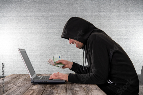 hacker in black hoody with laptop and euro notes