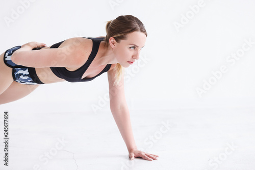 Beautiful young girl in a tracksuit doing exercises for the muscles of the hands and the press in the white gym against the background of sports equipment