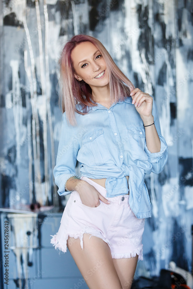 Fototapeta premium Vertical portrait of pleasant-looking caucasian female with pinkish hairstyle, wearing blue jeans casual shirt and shorts looking happily in camera. People, lifestyle, youth and happiness concept.