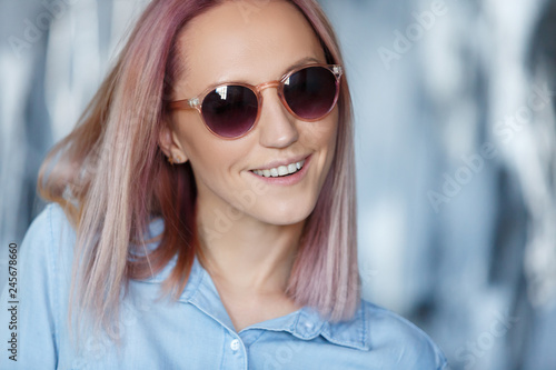 Close-up portrait of a charming hipster student in sunglasses with pink hair in a jersey shirt. Cute young girl in stylish modern clothes posing in studio